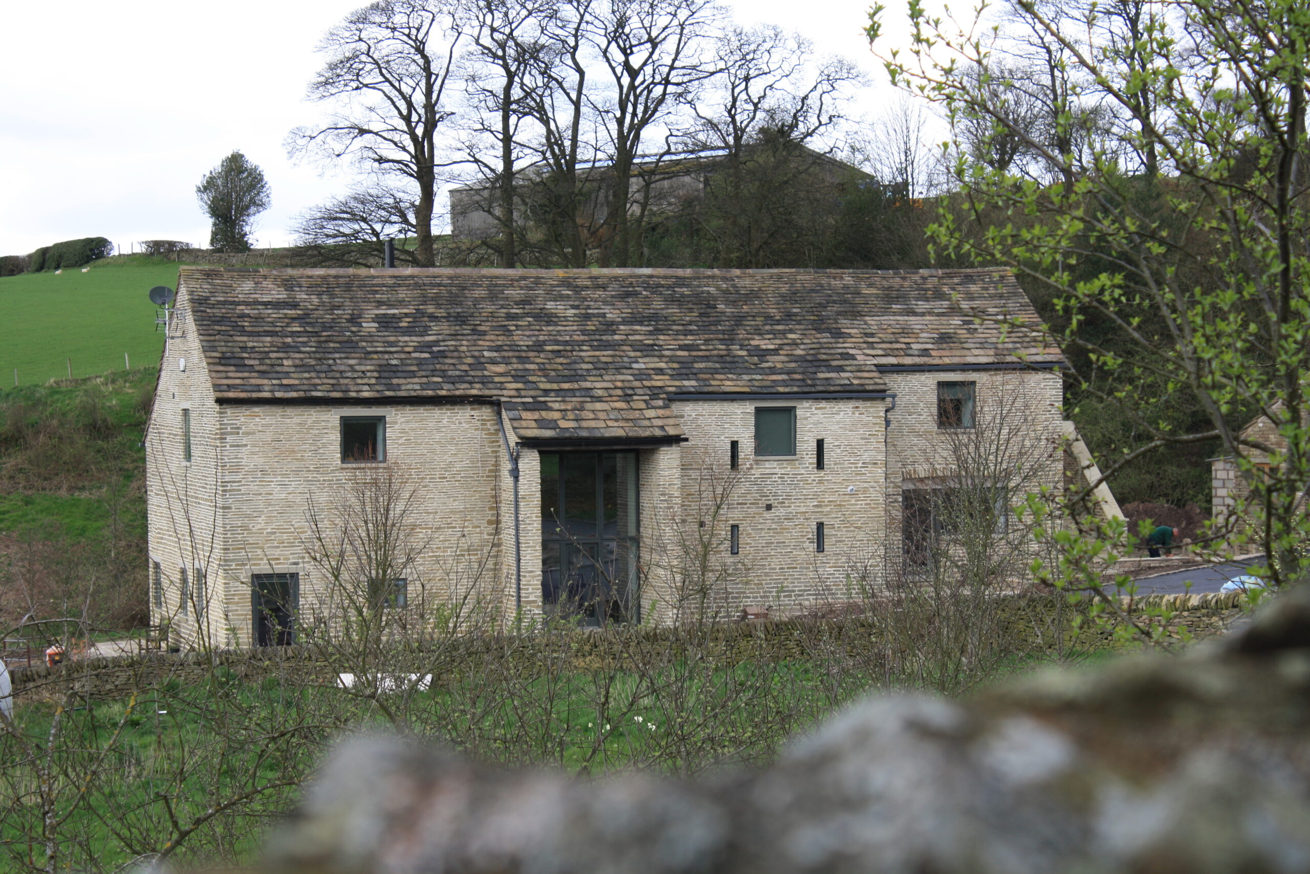 view of converted listed stone barn from a distance showing large double height glazed opening and retained barn opening