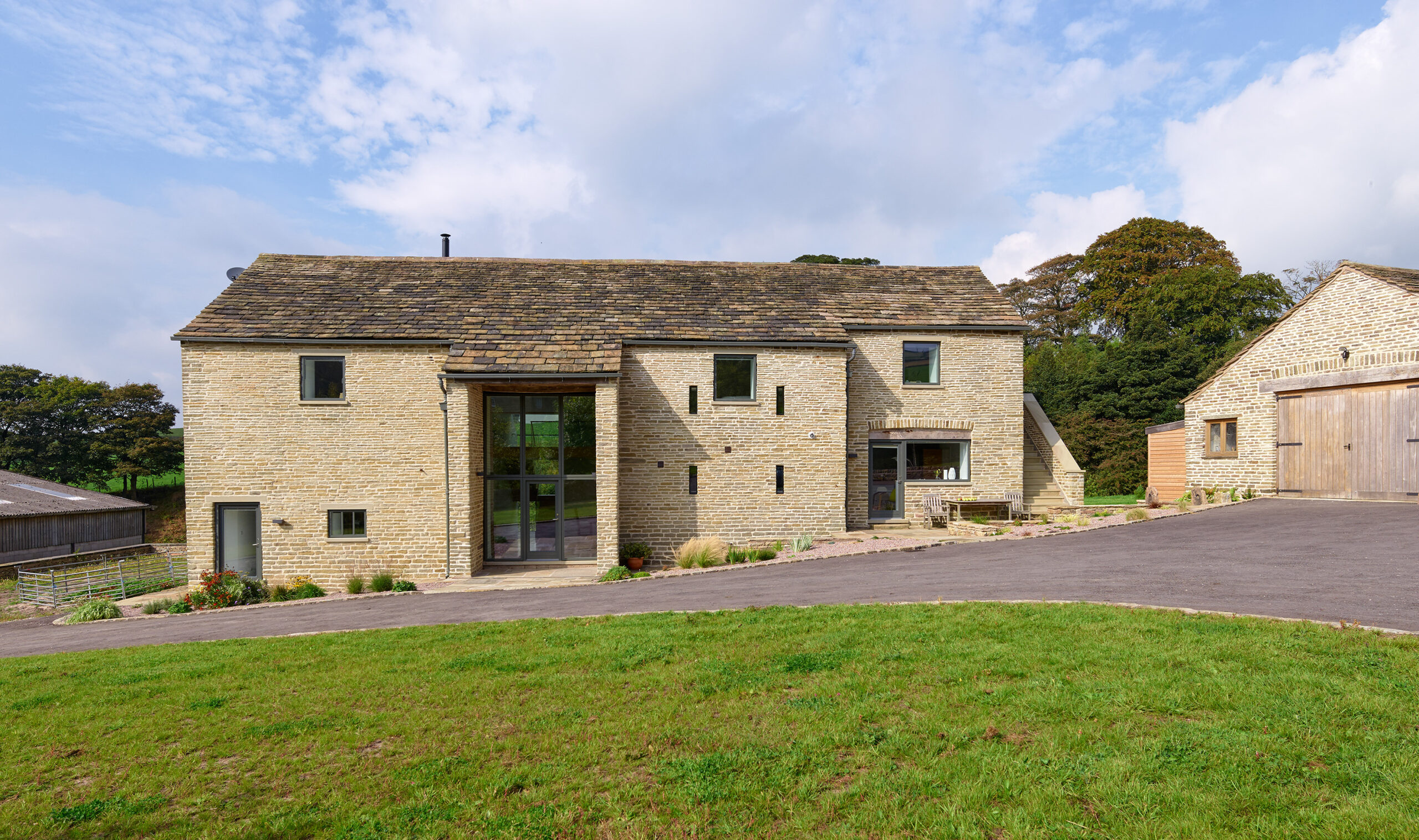 stone barn conversion listed building with large glass openings, sloped driveway leading to stone garage