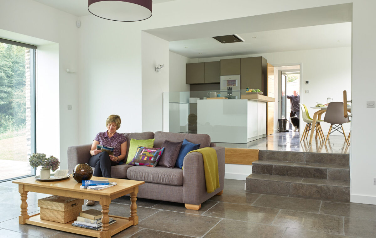 woman reading in the living area of the barn conversion with steps up into the kitchen