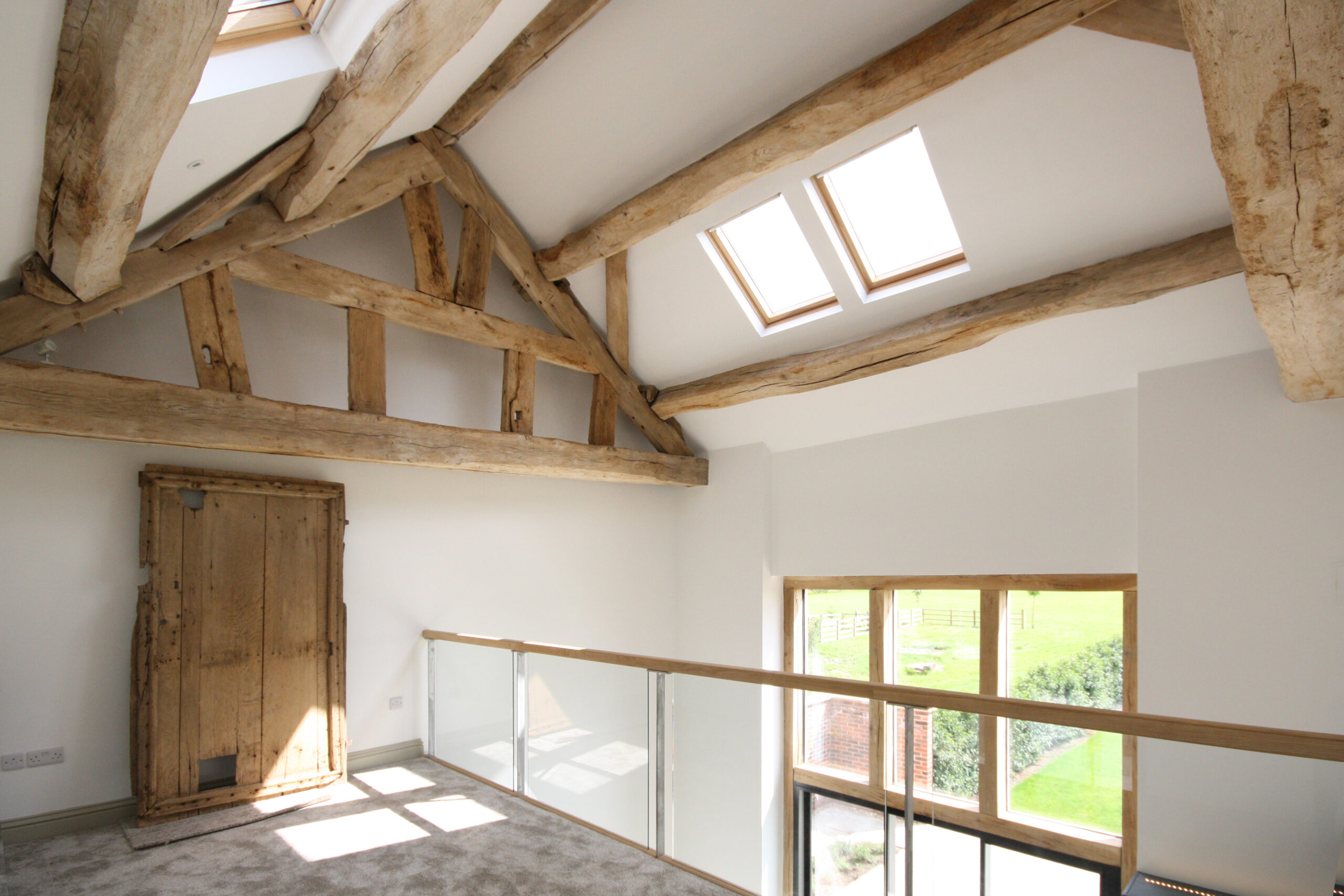 exposed original timber frame structure with mezzanine looking over onto open plan living space. large opening and rooflights provide natural light