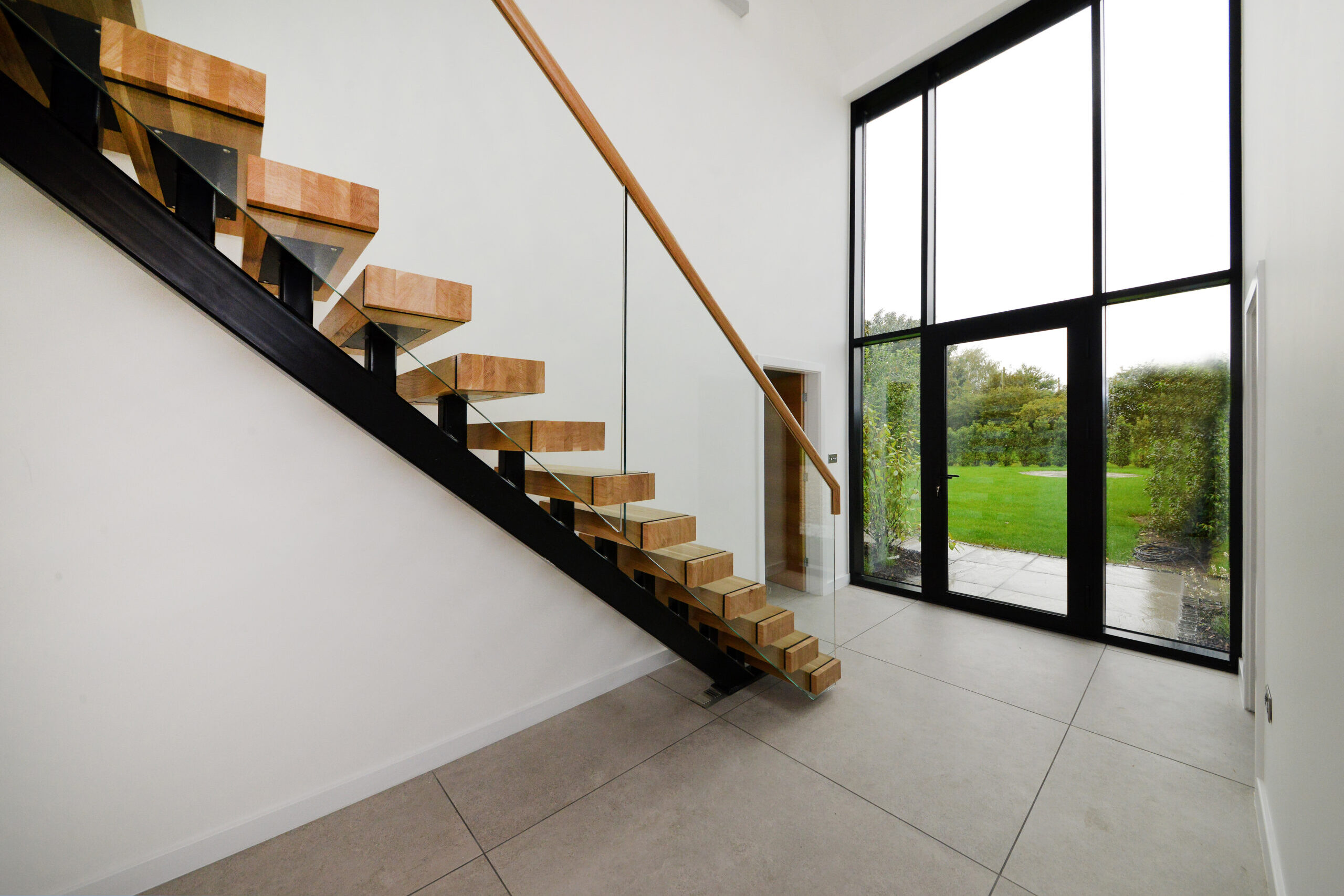double height glazing and timber staircase with glass balustrade in the entrance hall at New Orchard Barn