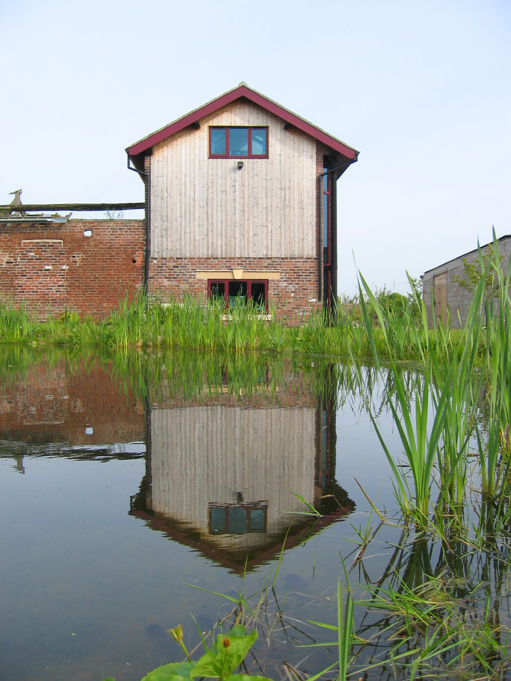 Gable end view of Beech Farm barn conversion with weathered timber cladding from across the lake