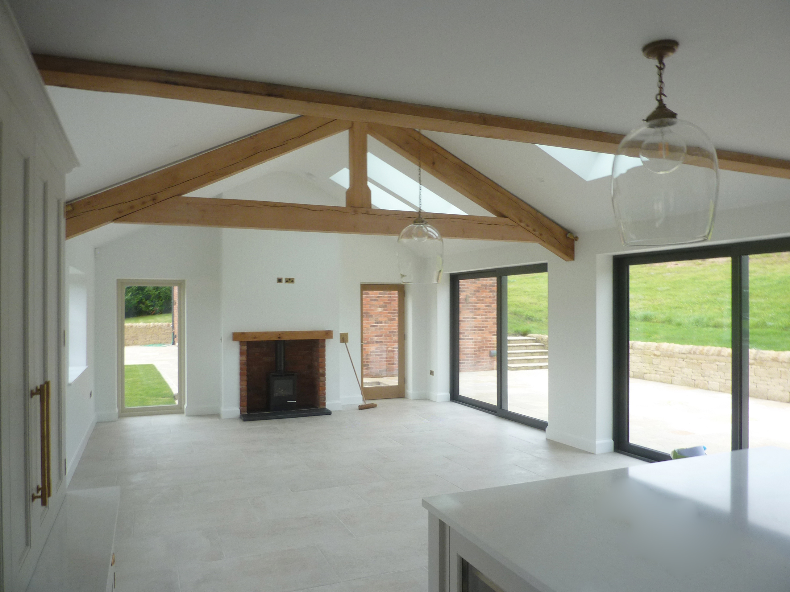 Open plan living space at Hazelwall Cottage with exposed roof truss, sliding patio doors and wood burning stove