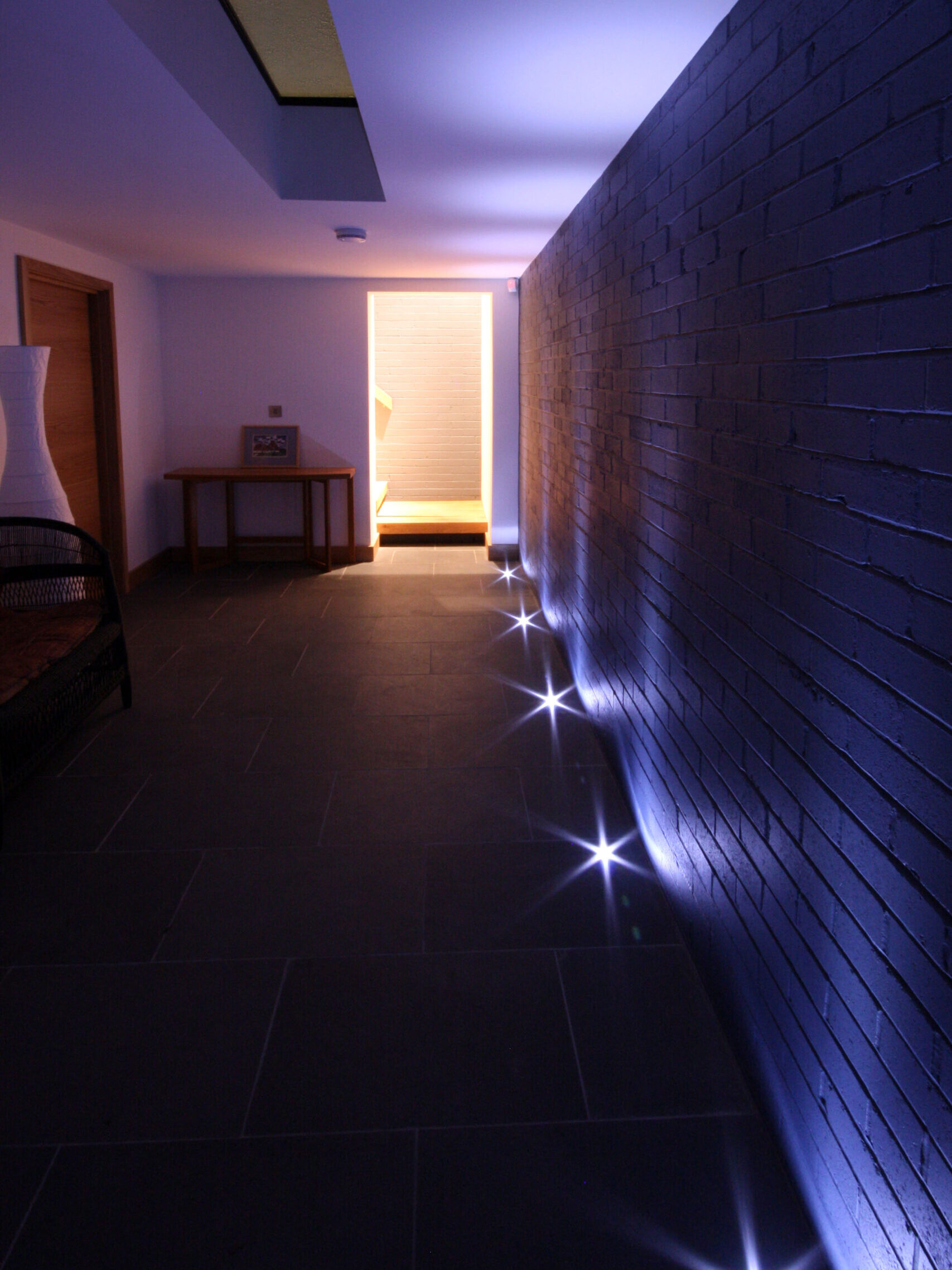 basement hallway with floor uplights highlighting the exposed painted brick with walk-on rooflight above