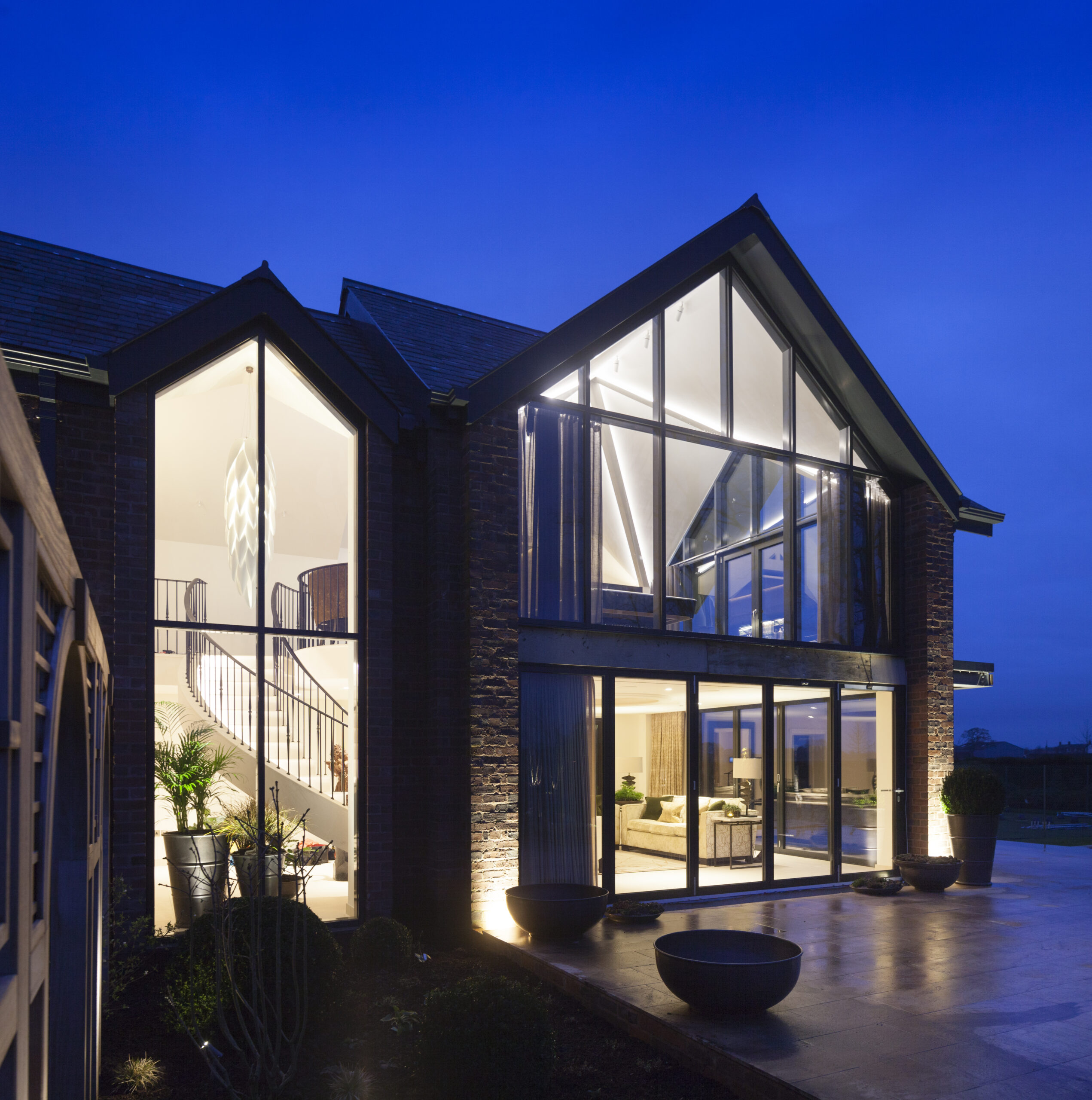 Evening shots of garden room and games room extension at Ash House with large double height glazing exposing stone staircase