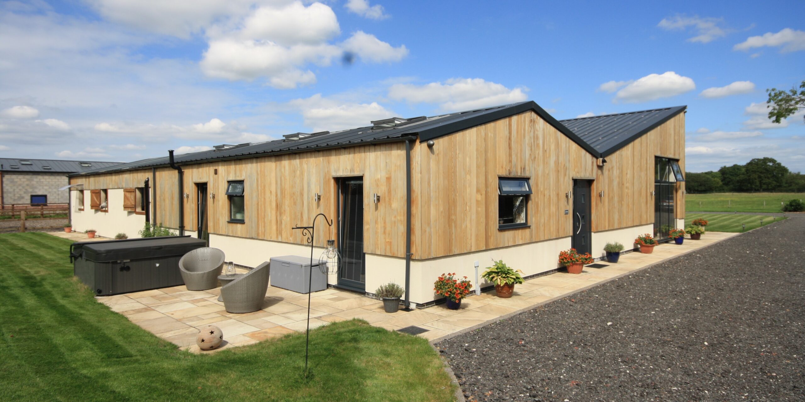 vertical timber cladding, low level render finish and sheet metal roof covering to partial conversion of stables with Rear patio are and garden