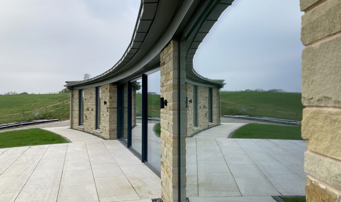Curved stone wall with overhanging zinc roof and full height glazing