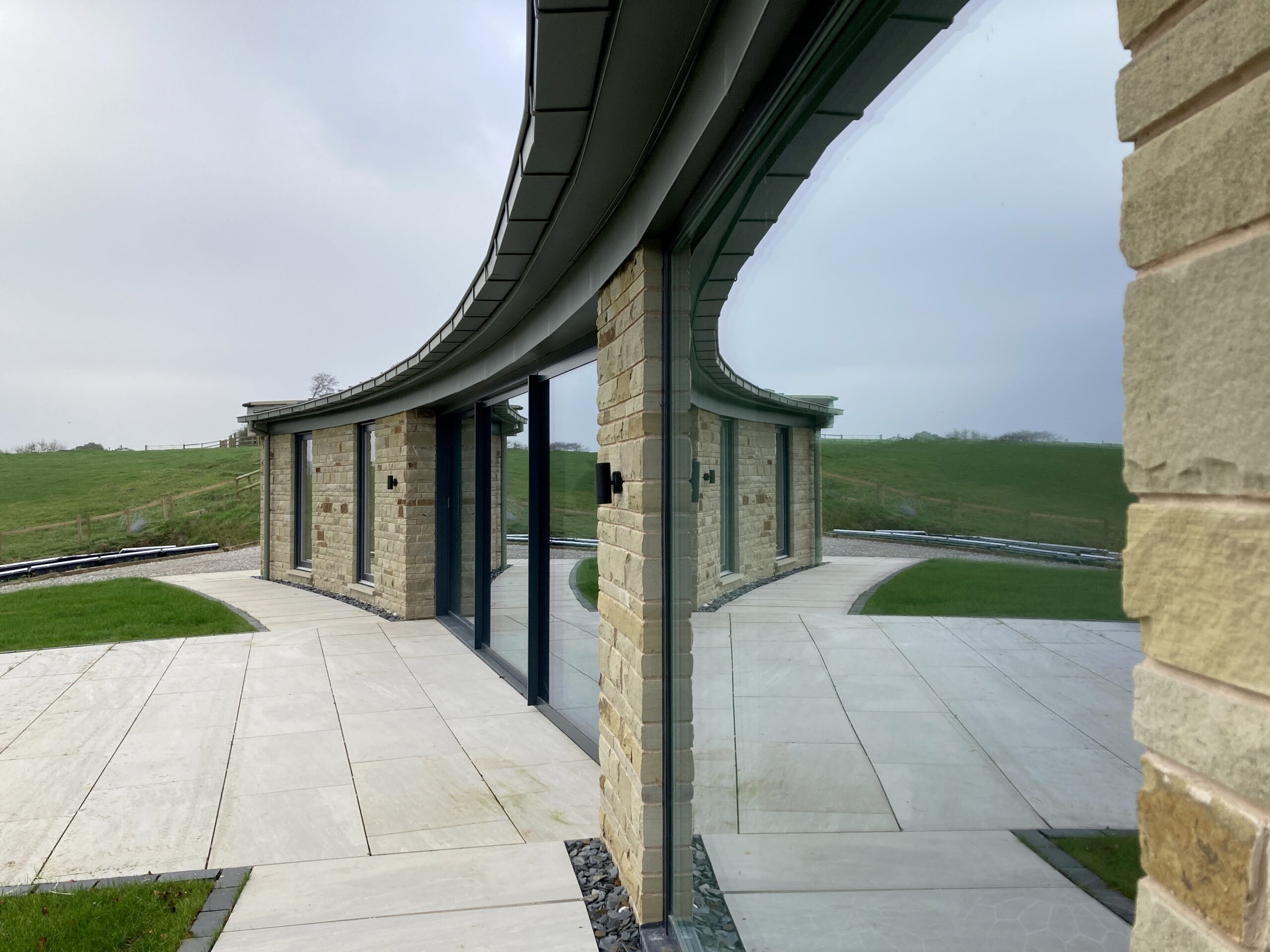 Curved stone wall with overhanging zinc roof and full height glazing
