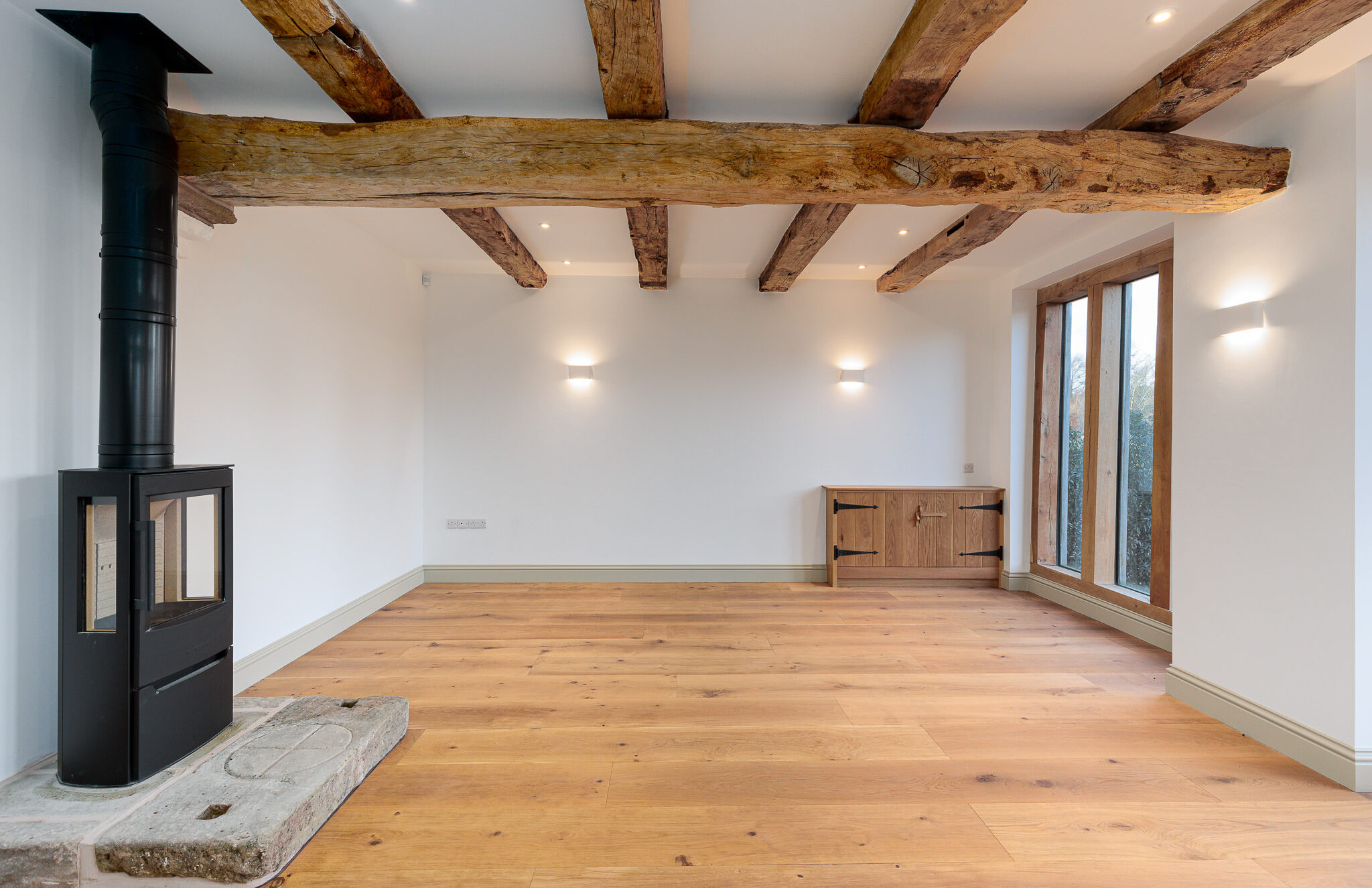 sitting room with exposed retained timber floor joists and wood burning stove on stone hearth