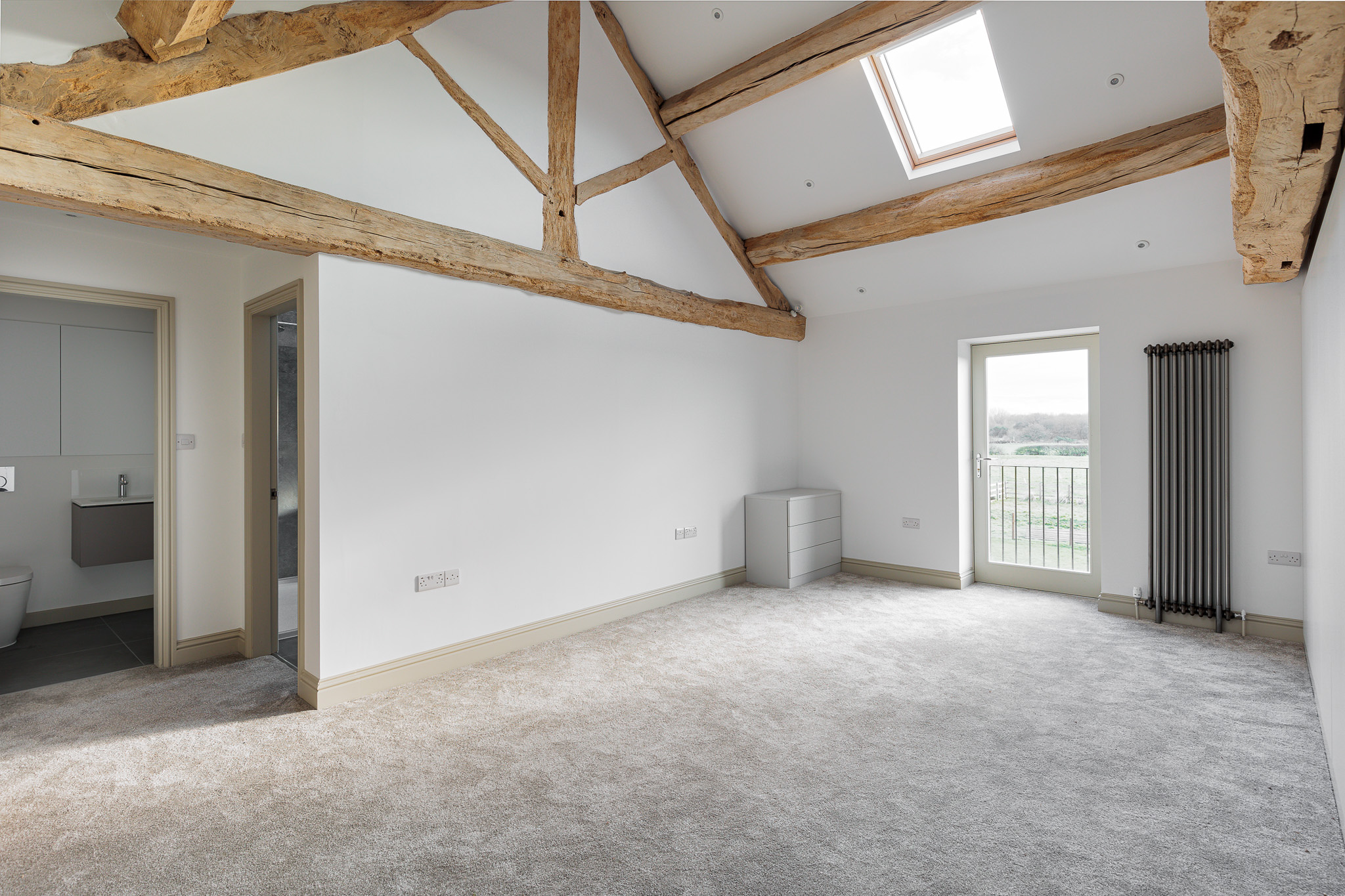 bedroom with exposed retained oak trusses and roof purlins with new rooflight and door opening onto juliet balcony