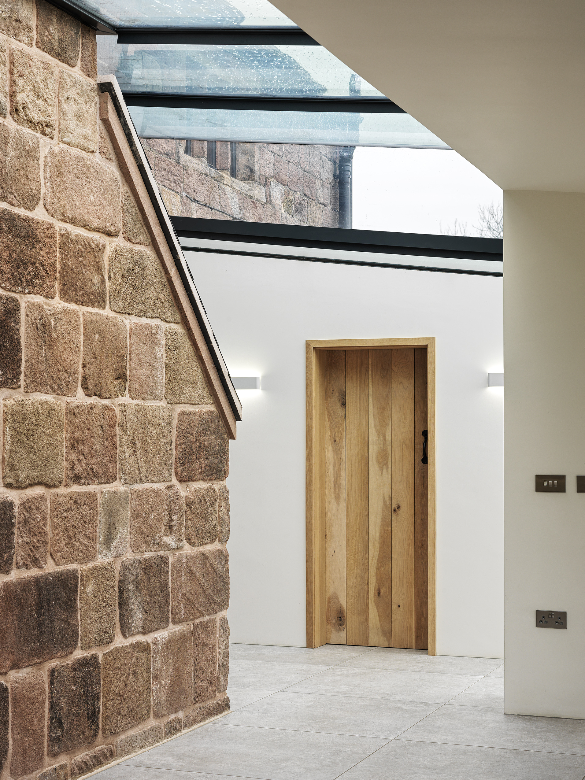 A new rear extension to a Grade 2 listed farmhouse with exposed original stonework of the farmhouse. Large roof glazing over the entrance hall and surrounding the original chimney. Solid timber panelled doors and architraves