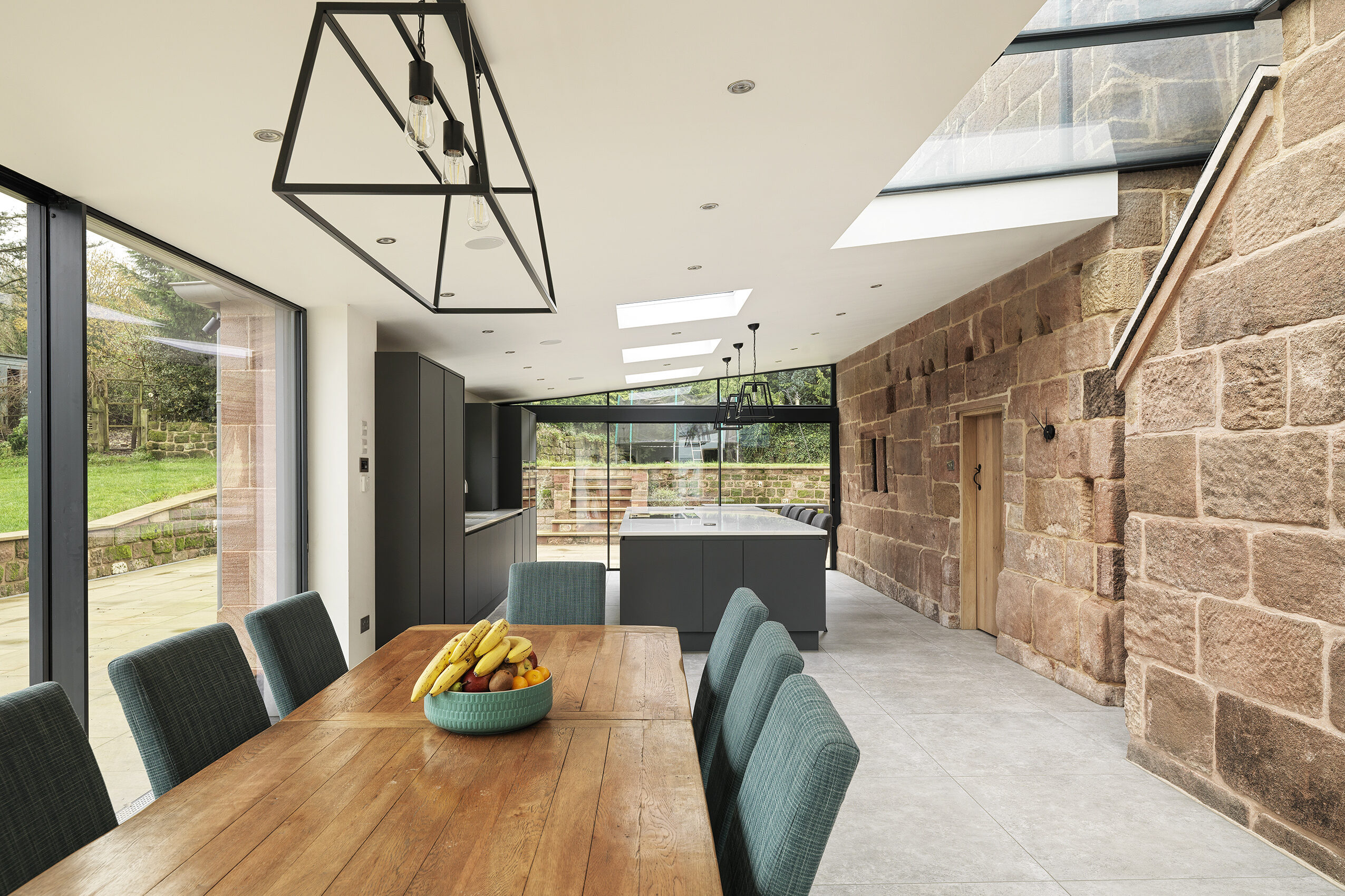 A new kitchen and dining rear extension to a Grade 2 listed farmhouse with large floor to ceiling openings and large roof glazing and rooflights allowing natural light into the new, modern space with sunlight washing over the exposed original stonework