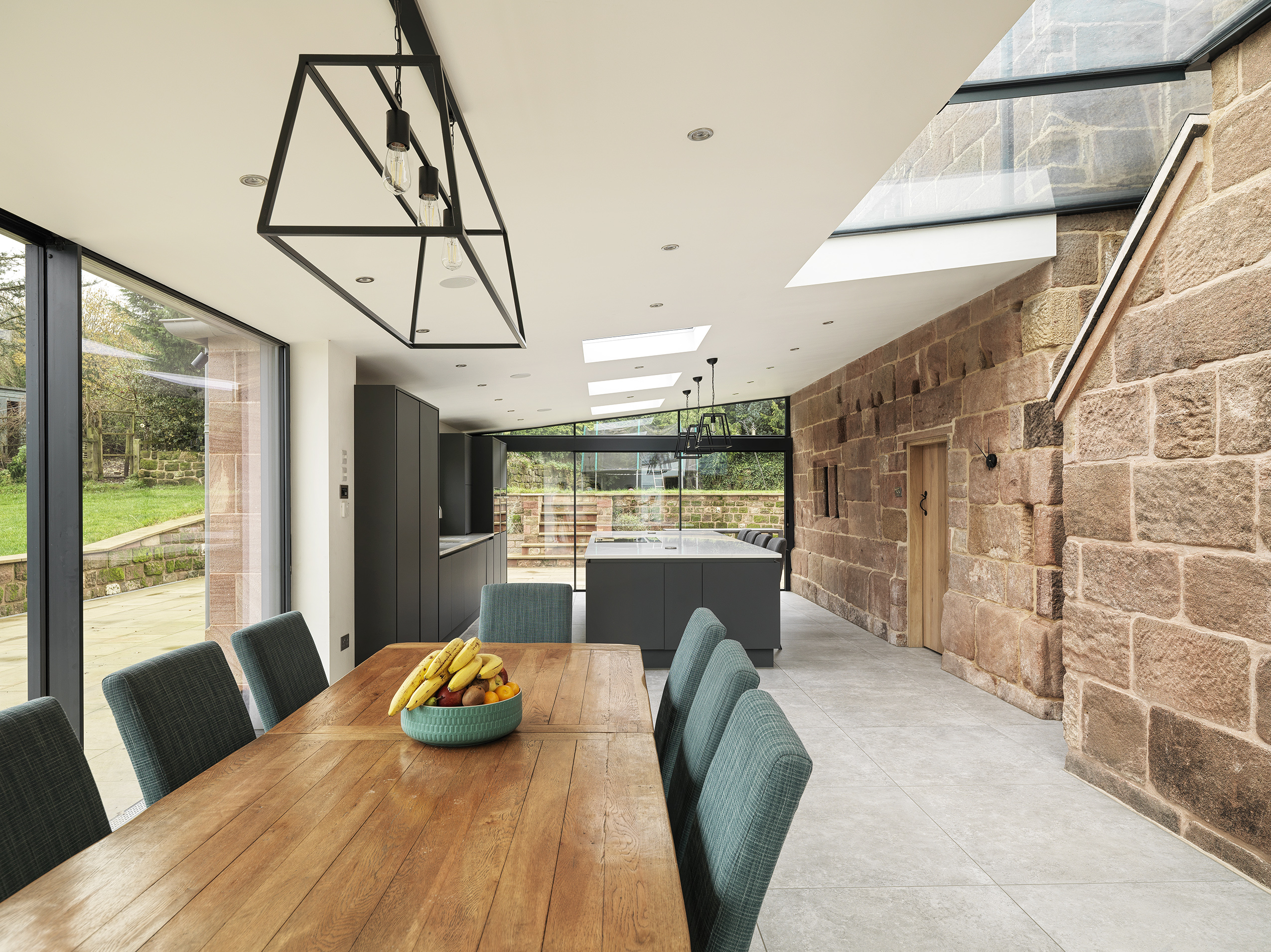 A new kitchen and dining rear extension to a Grade 2 listed farmhouse with large floor to ceiling openings and large roof glazing and rooflights allowing natural light into the new, modern space with sunlight washing over the exposed original stonework