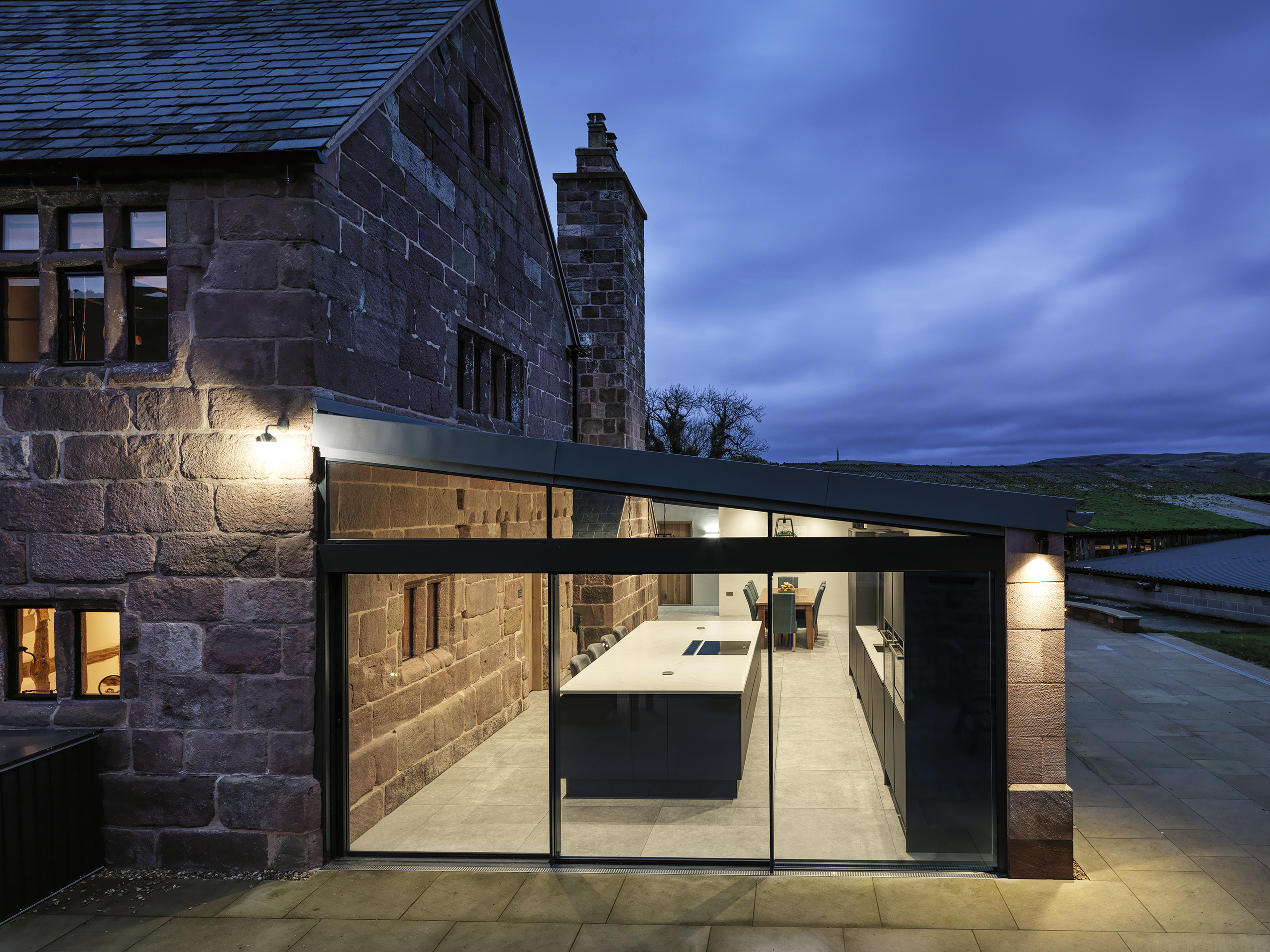 side elevation of a new single storey rear extension to a Grade 2 listed farmhouse with full height glazed openings providing views into highlighting the original exposed stonework with spotlights highlighting key features
