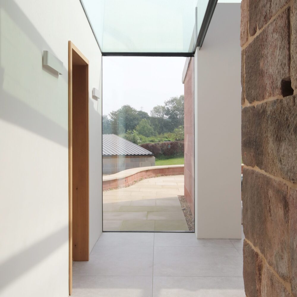 Thin framed full height glazing with glazed ceiling linking grade 2 listed farmhouse with a new modern open plan living extension offering views to agricultural buildings and farm land beyond.