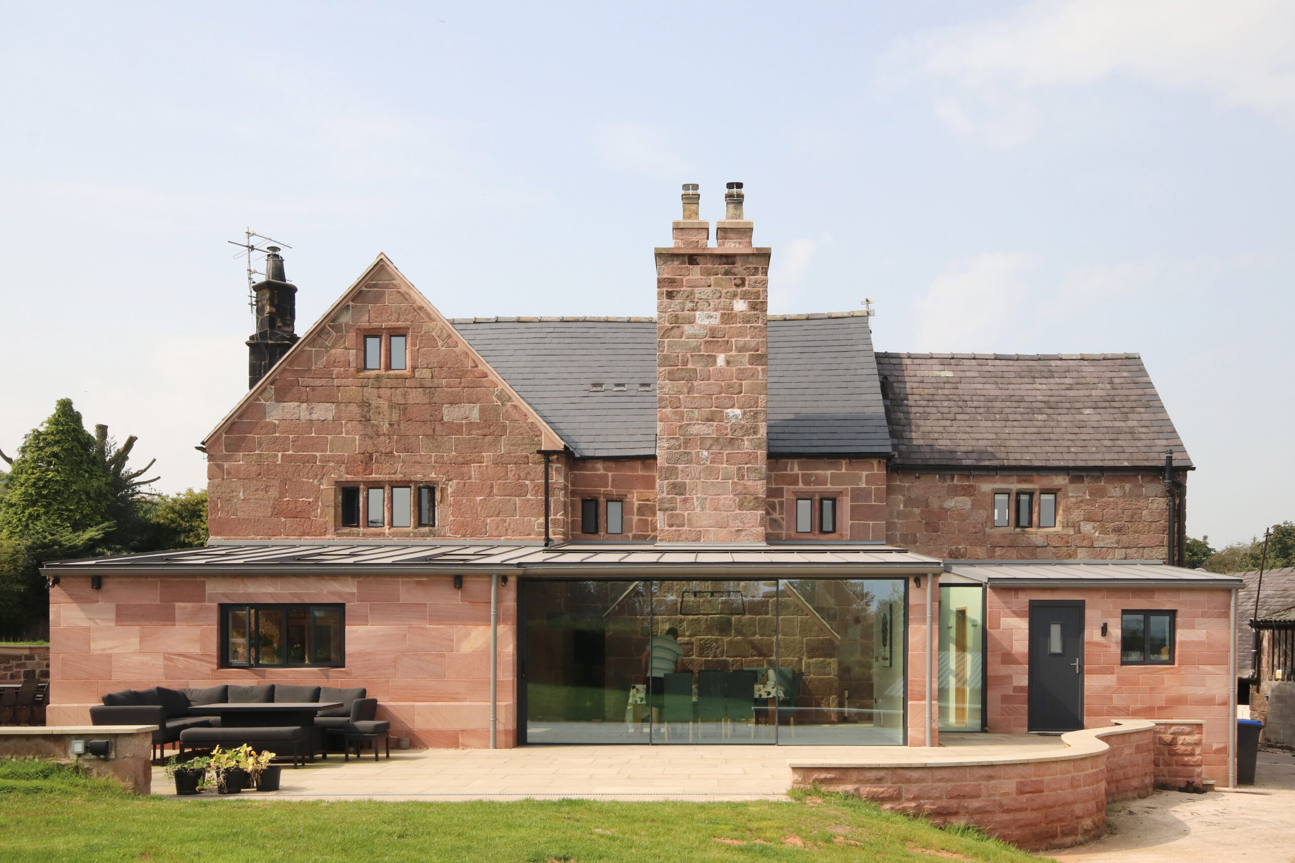 New single storey modern stone rear extension to a grade 2 listed stone farmhouse with low pitched zinc cladding and large glazed opening and roof glazing