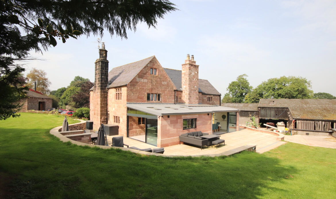 Grade 2 listed stone farmhouse with modern, lean-to extension with low pitched zinc roof. Large glazed openings on the 2 elevations opening onto a new patio area and retaining walls forming the landscaped area beyond