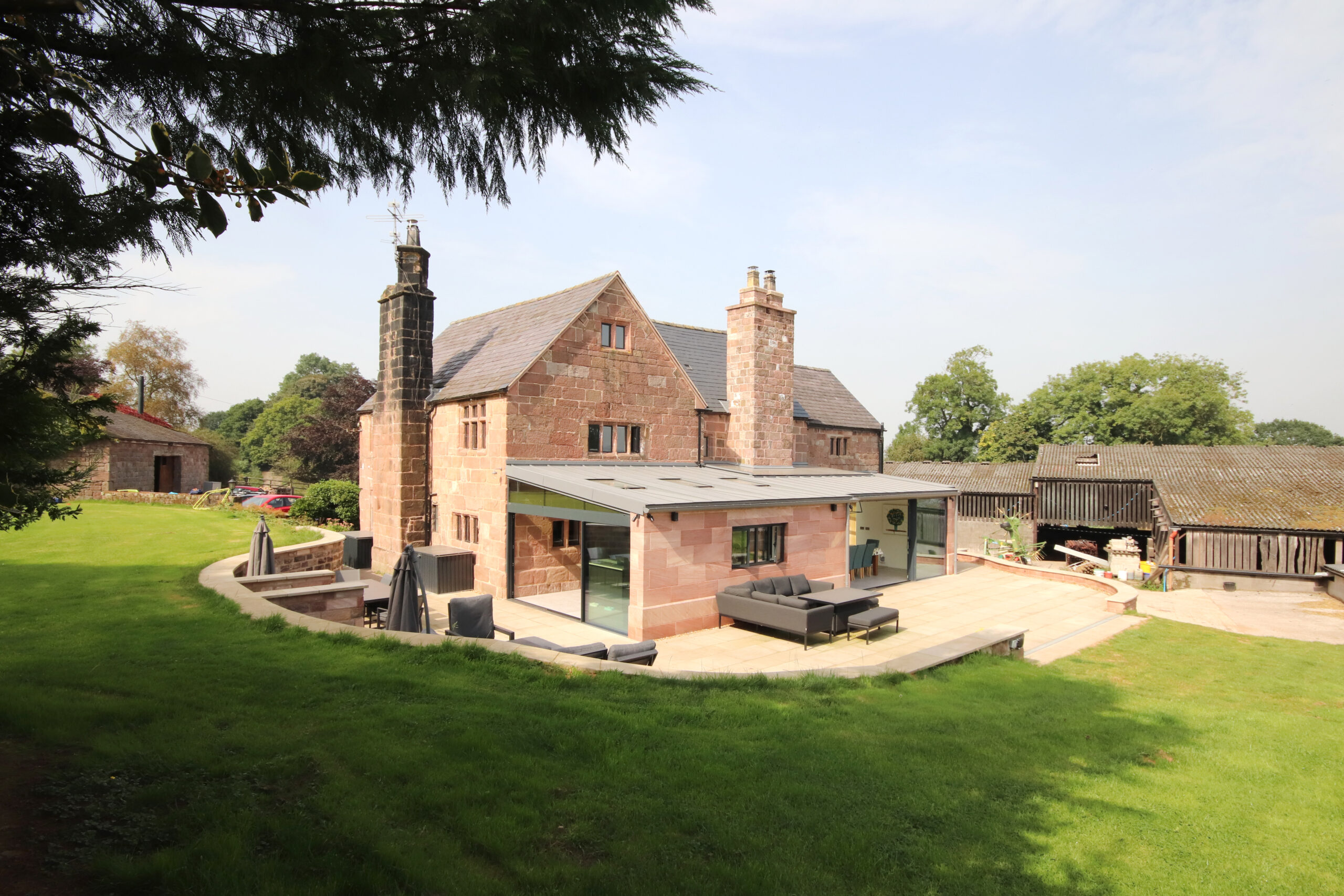 Grade 2 listed stone farmhouse with modern, lean-to extension with low pitched zinc roof. Large glazed openings on the 2 elevations opening onto a new patio area and retaining walls forming the landscaped area beyond
