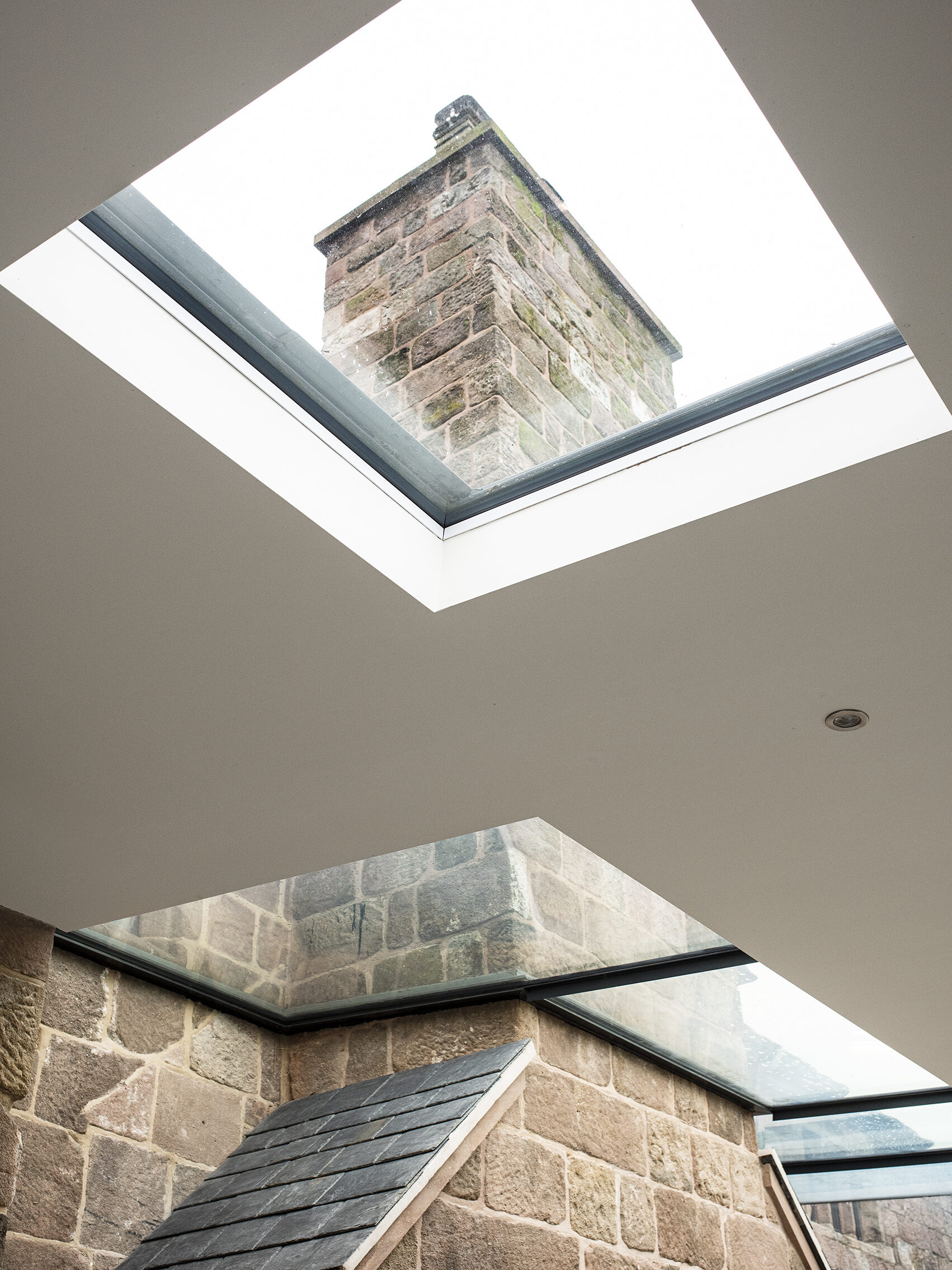 Large rooflights and roof glazing in a new single storey rear extension to a Grade 2 listed farmhouse framing the renovated stone chimney of the original dwelling