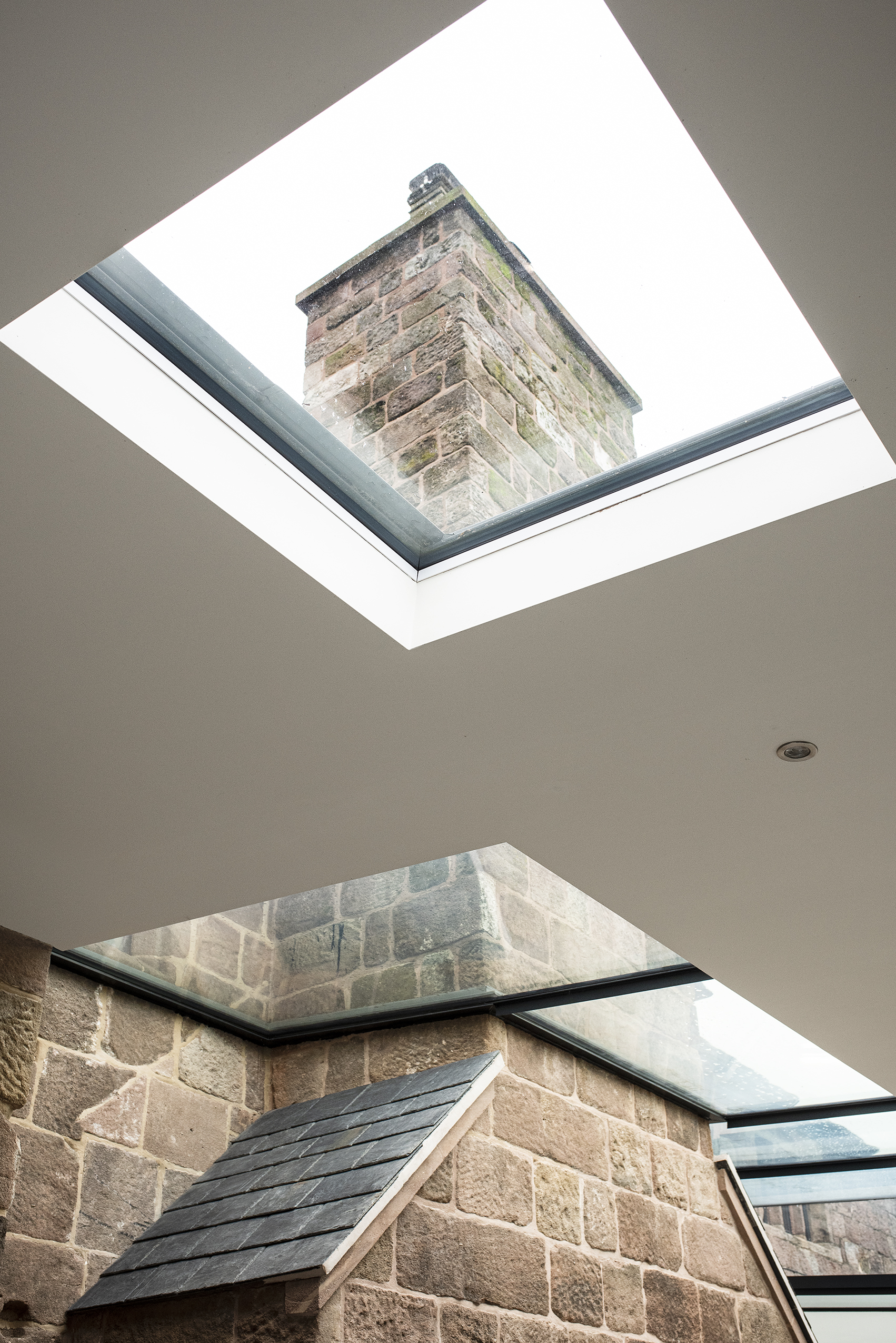 Large rooflights and roof glazing in a new single storey rear extension to a Grade 2 listed farmhouse framing the renovated stone chimney of the original dwelling